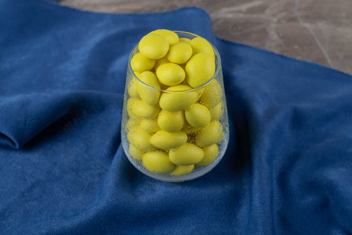 好吃的装满黄色口香糖的玻璃杯 在毛巾上 在大理石表面配料口香糖杯子