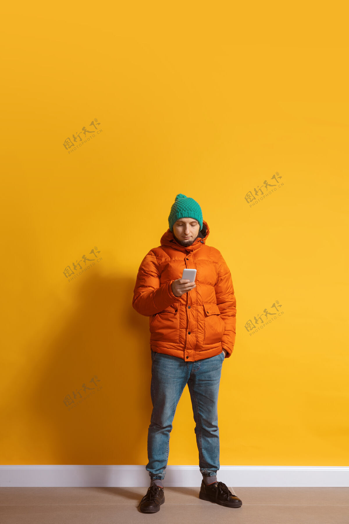 照片年轻的白人男子用智能手机全身肖像隔离在黄色的墙壁白种人手时尚