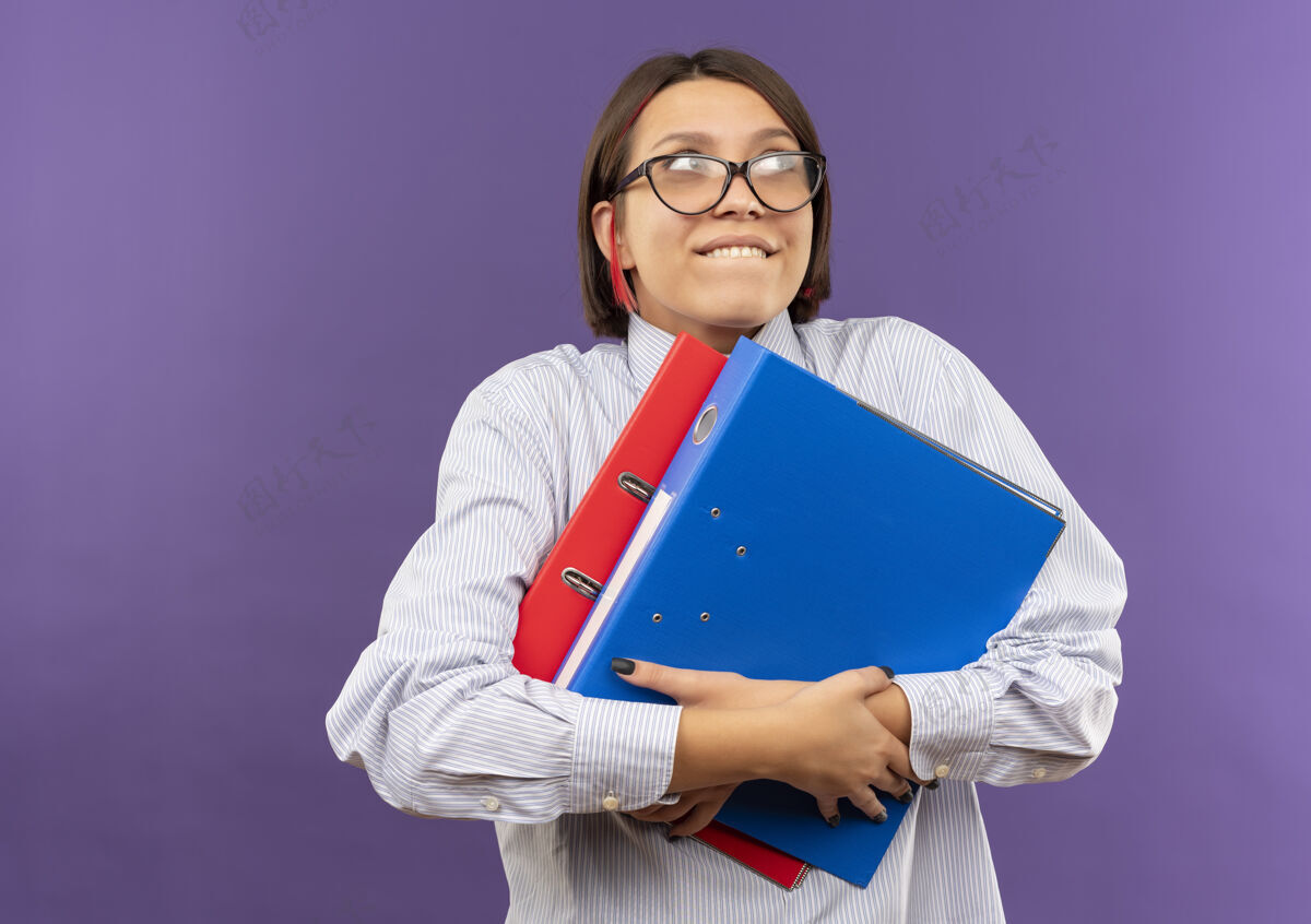 中心高兴的年轻呼叫中心的女孩戴着眼镜拿着文件夹看着一边孤立的紫色背景与复印空间请戴眼镜壁板