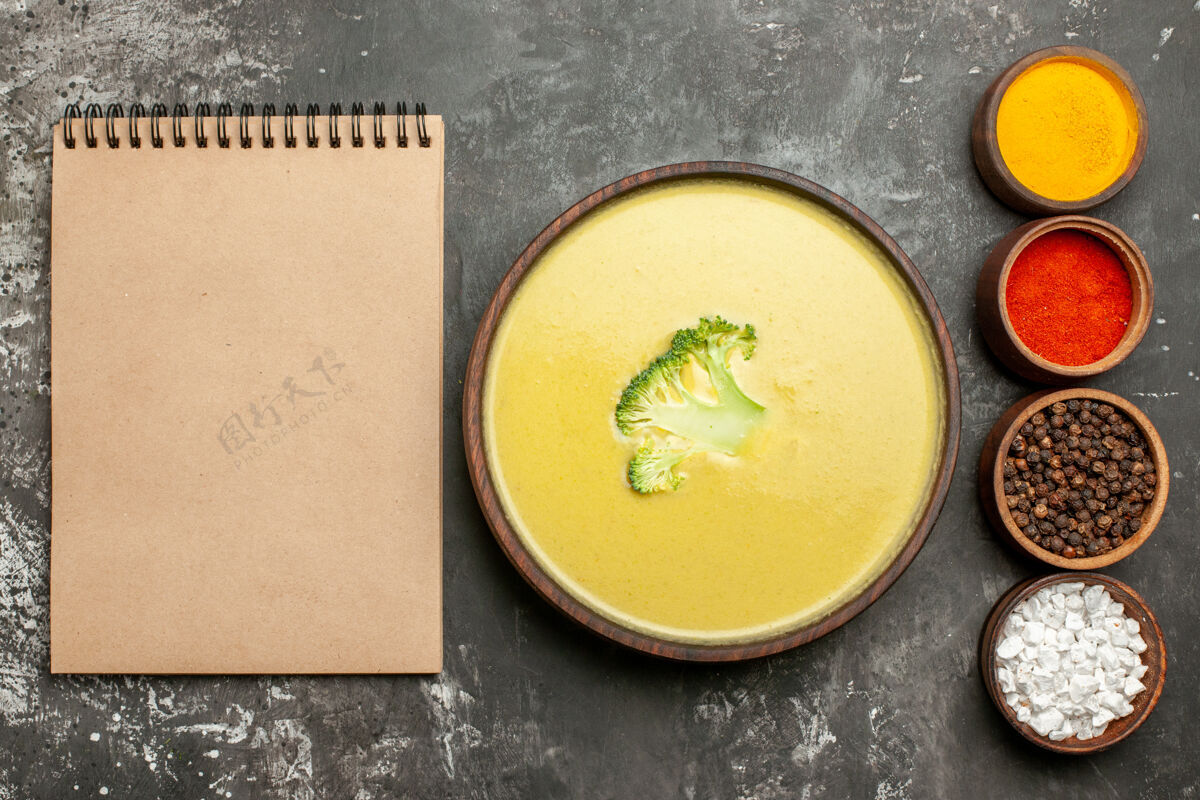 餐奶油西兰花汤在一个棕色的碗和不同的香料旁边的笔记本在灰色的桌子上盘子不同香料