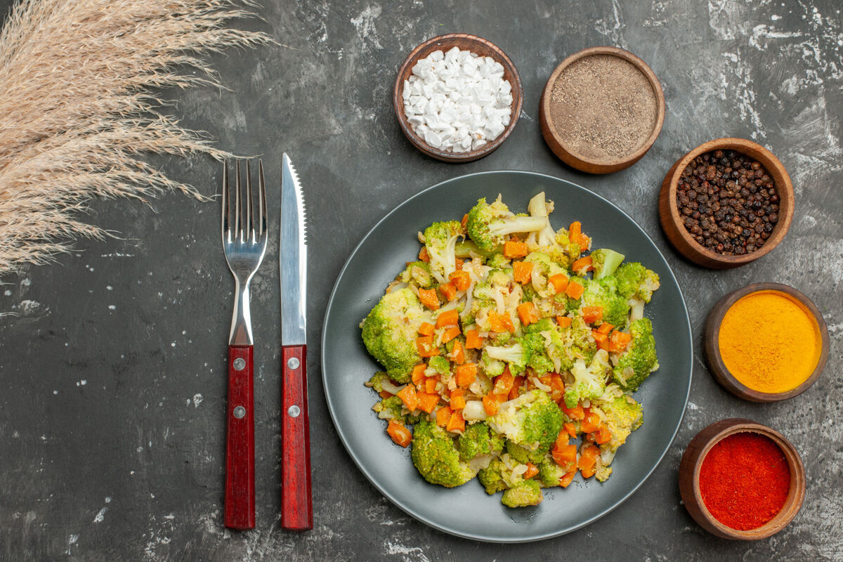 农产品上图：健康膳食 黑色盘子上放着花椰菜和胡萝卜 灰色桌子上放着香料晚餐花椰菜肉