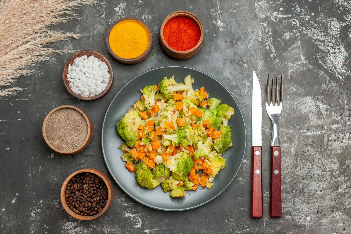 午餐健康餐 黑盘子上放花椰菜和胡萝卜 灰色桌子上放香料餐厅胡萝卜花椰菜
