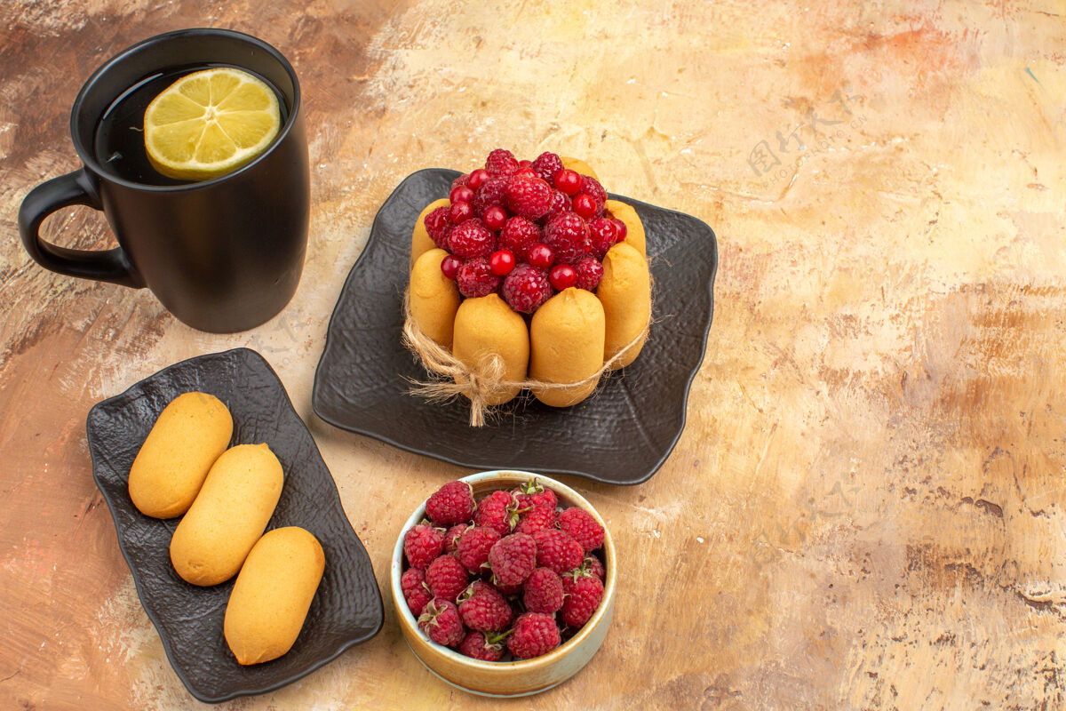 草莓一个礼品蛋糕和茶放在一个黑杯子里 柠檬和饼干放在五颜六色的桌子上可食用水果饮食健康