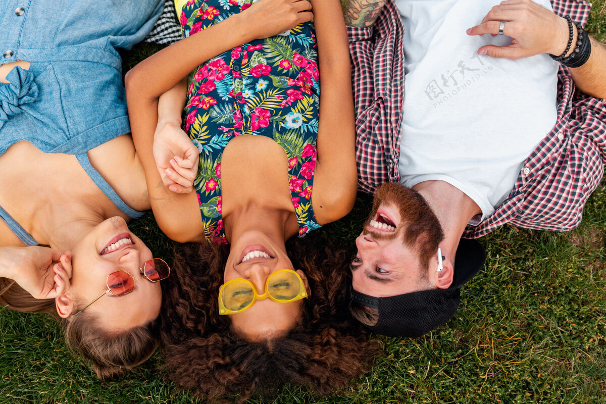 年轻俯瞰五颜六色时尚快乐的年轻朋友们躺在公园的草地上 男女同乐人太阳镜在一起
