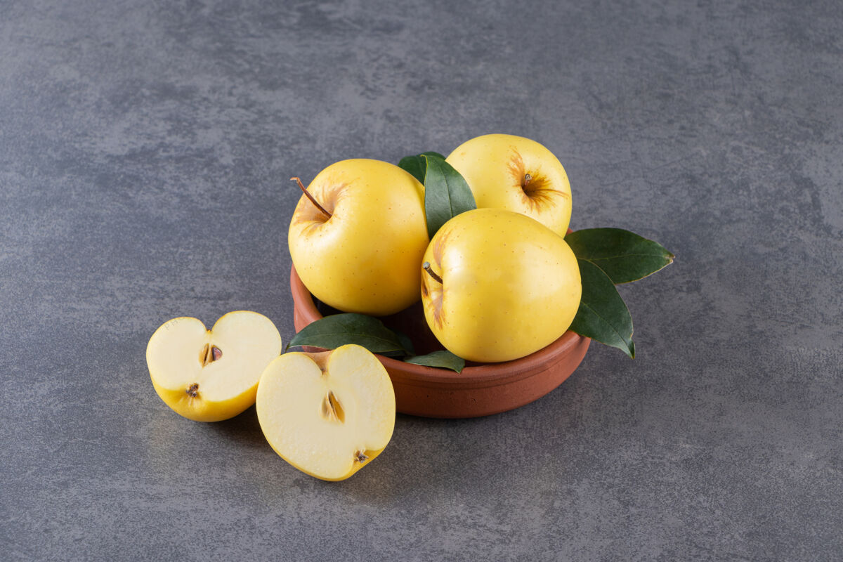 切片成熟的黄苹果和绿叶放在泥碗里成熟叶健康