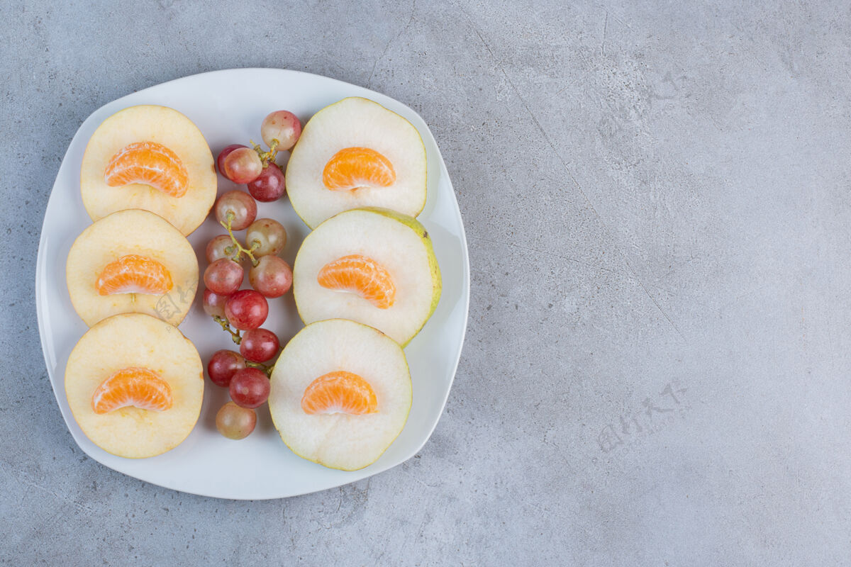美味把苹果 梨 橘子和葡萄片放在大理石背景上的盘子里配料风味健康