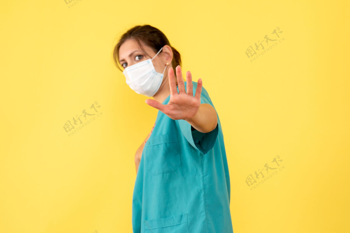 手持前视图黄色背景上穿着医用衬衫和面罩的女医生成人大流行面具