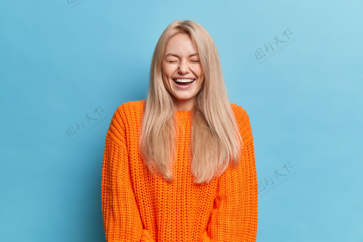 积极喜出望外的金发女人笑得很开心听到一些有趣的事情闭上眼睛显示白色牙齿穿着橙色针织毛衣大笑休息美丽
