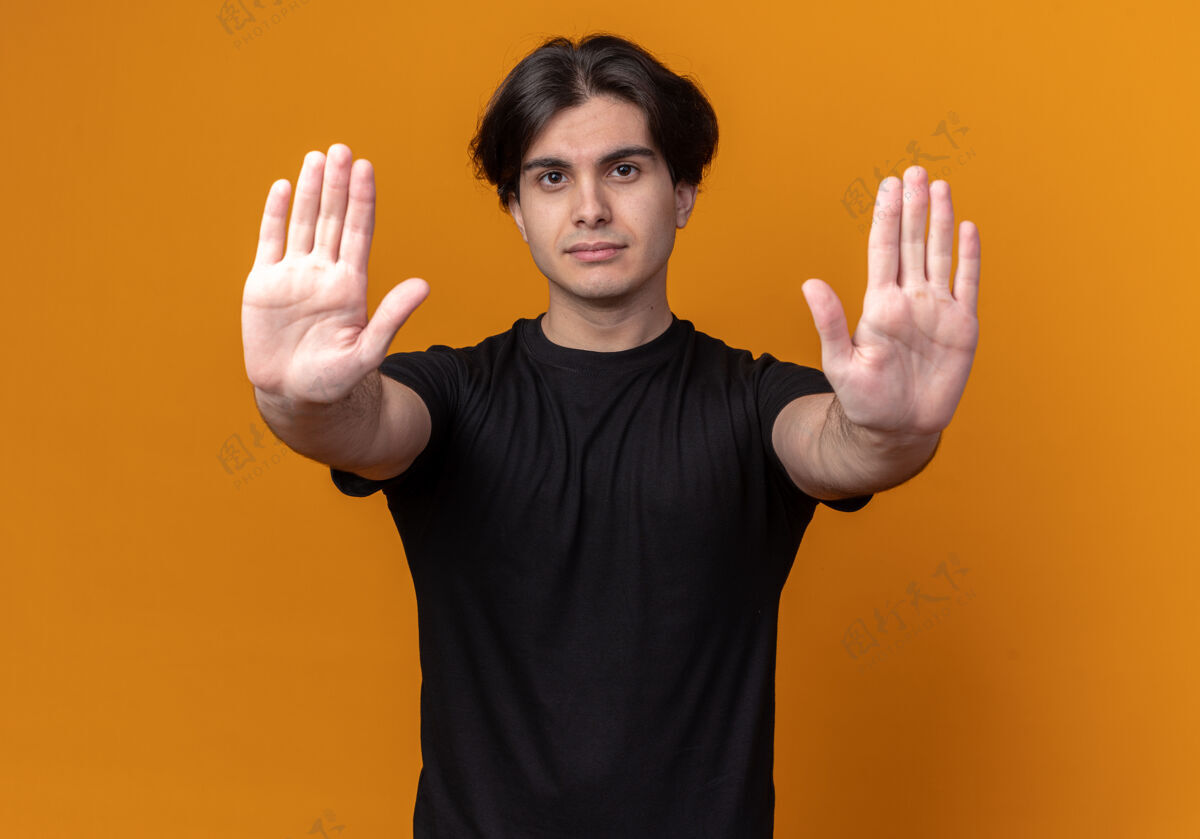 严格一个穿着黑色t恤的年轻帅哥 在橘色的墙上显示着停止的手势T恤停下年轻