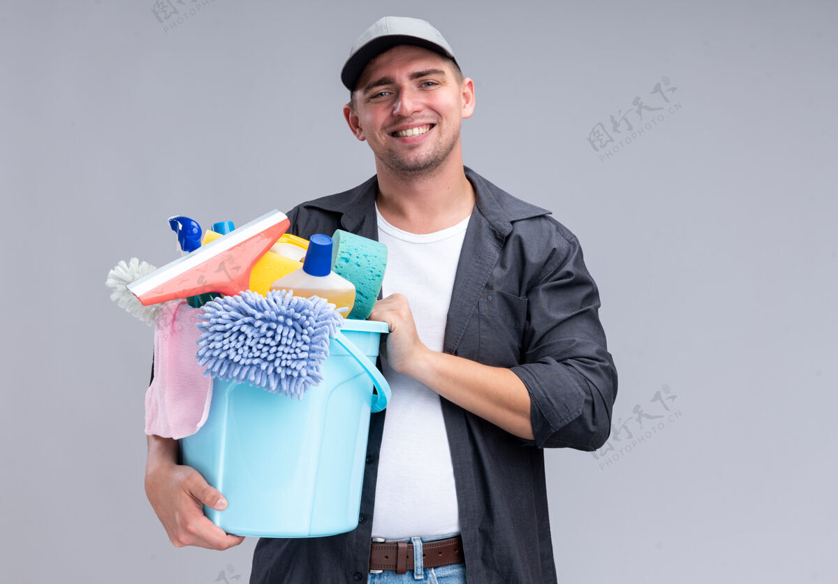 微笑面带微笑的年轻帅哥 穿着t恤 戴着帽子 手里拿着一桶清洁工具 隔离在白色的墙上 留着复印空间水桶帽子年轻人