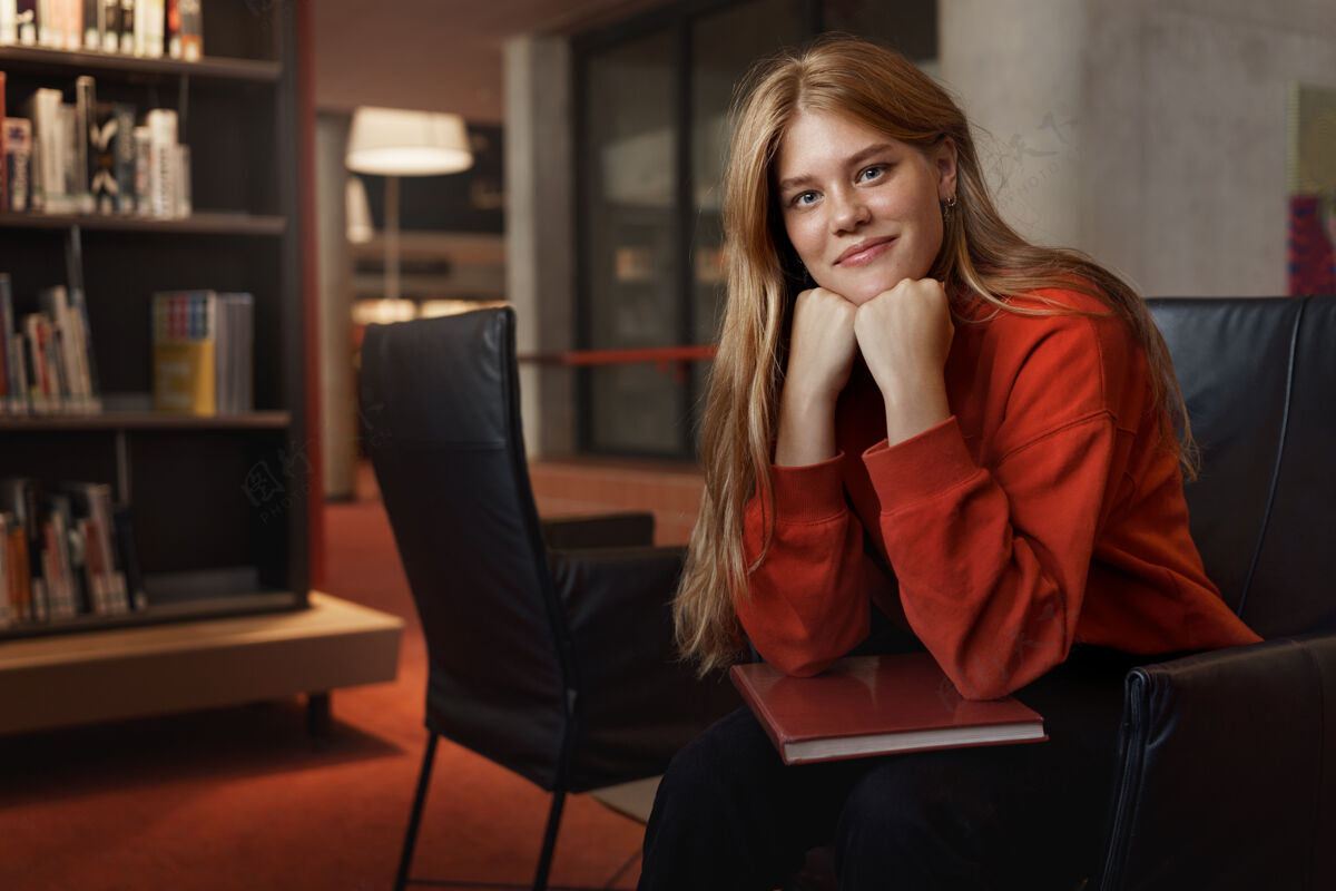 研究年轻漂亮的红发女学生的画像 坐在扶手椅上 靠在胳膊上微笑着阅读成人人
