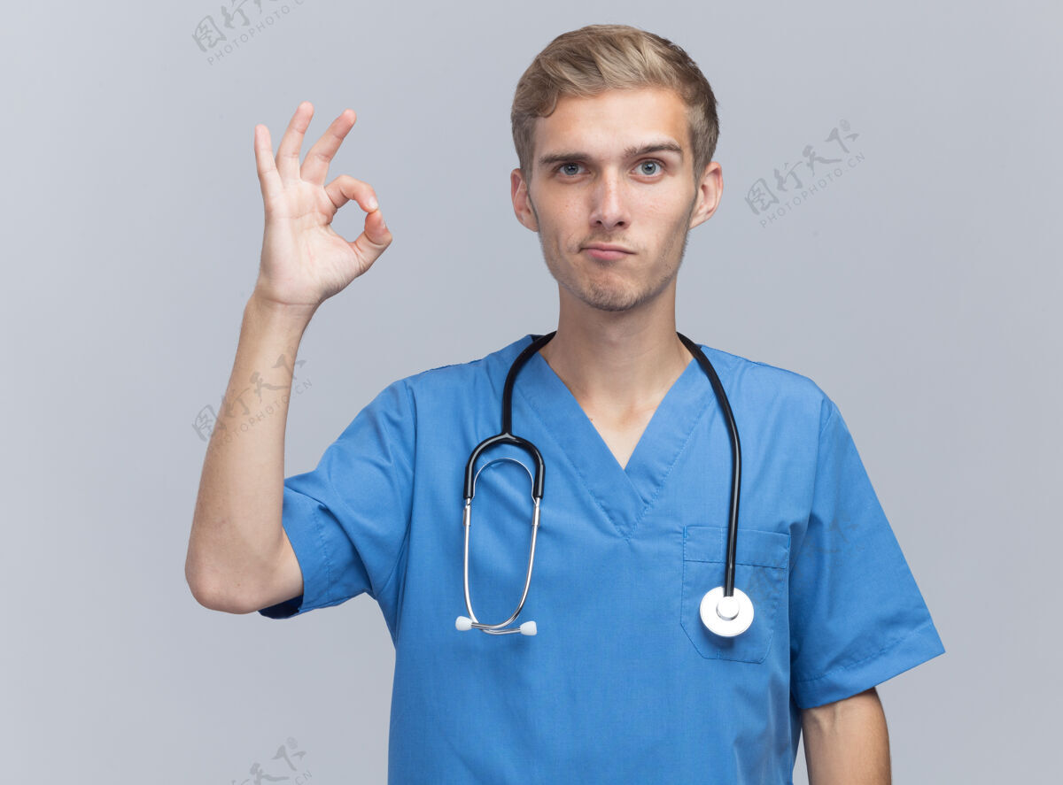 年轻高兴的年轻男医生穿着医生制服 听诊器显示出良好的姿态隔离在白墙上手势医生听诊器