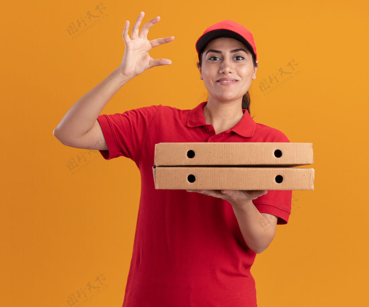拿着微笑着的年轻送货女孩穿着制服 戴着帽子 拿着披萨盒 在橘黄色的墙上显示大小隔离帽子女孩送货