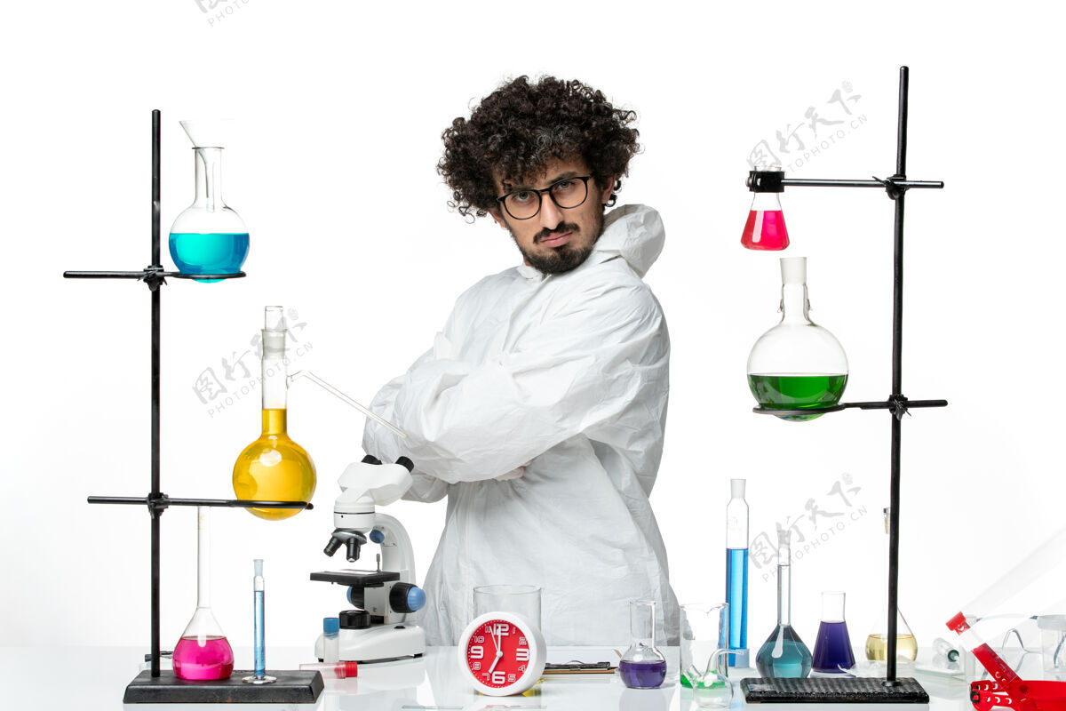 科学正面图身穿白色特殊套装的年轻男性科学家站在桌子旁 拿着解决方案溶液实验烧杯