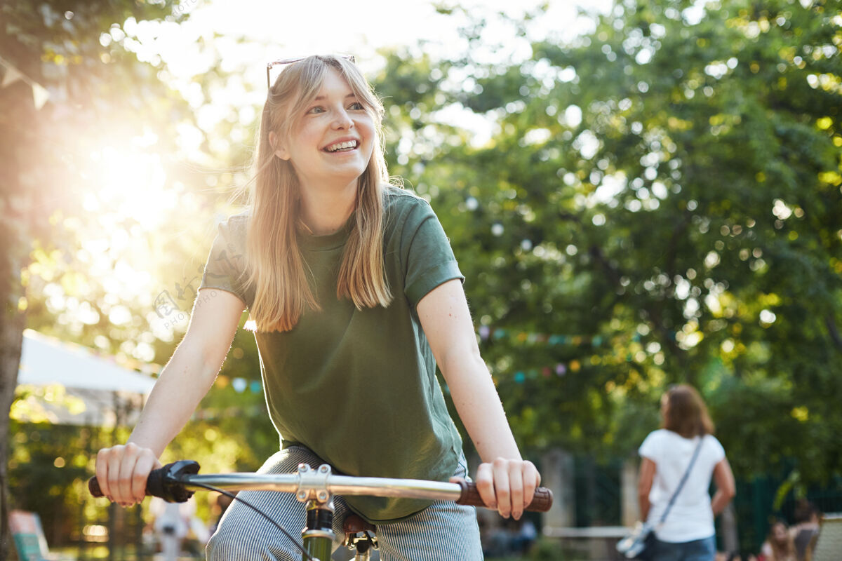 自行车在美食节期间 一位年轻漂亮的金发女郎在公园里假装骑自行车 这是一张照片绿色活跃乐趣