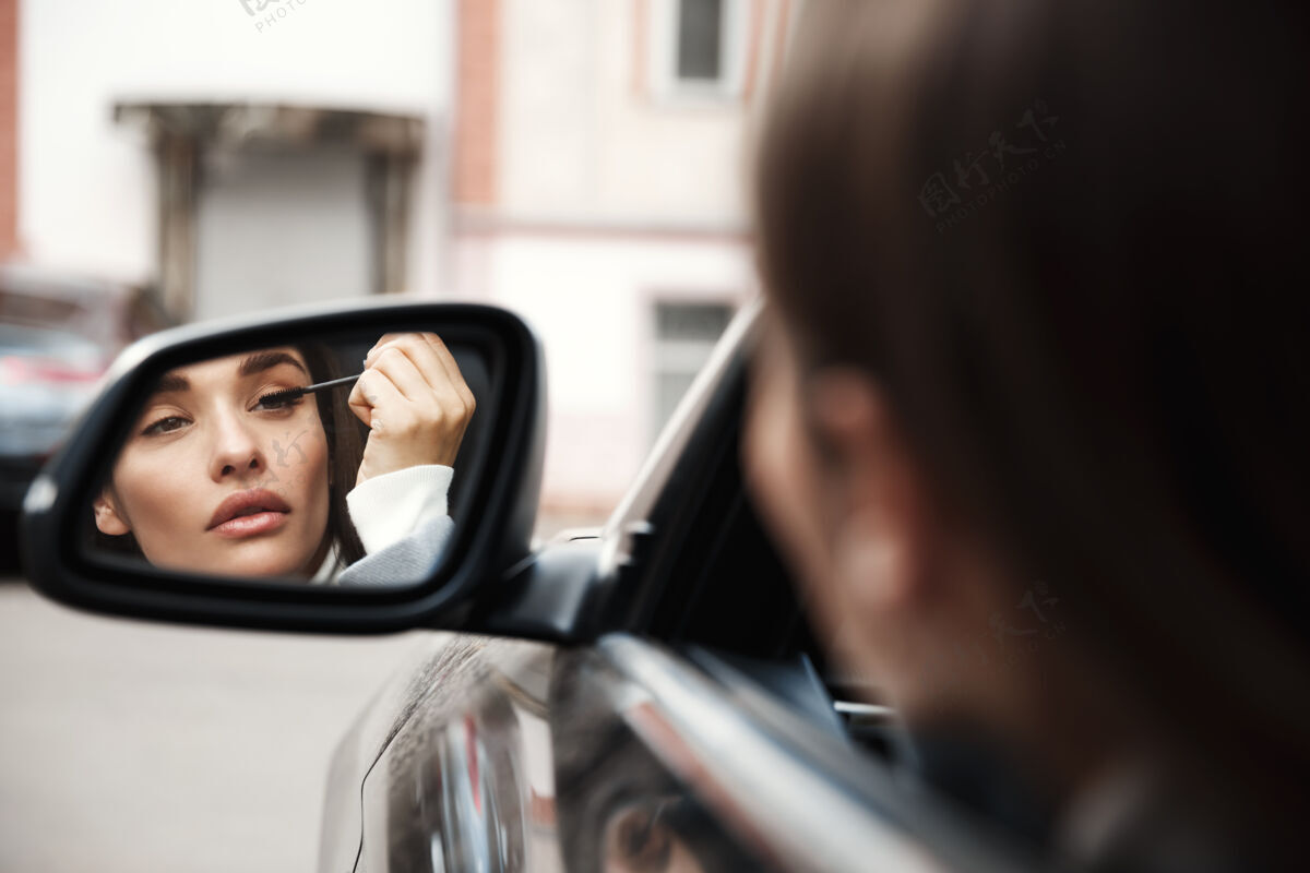 黑发坐在车里涂睫毛膏的女司机看着后视镜驾驶化妆旅程
