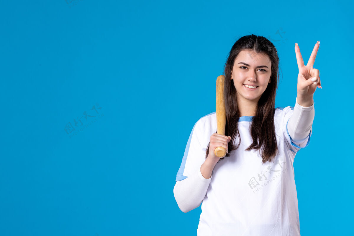 观点正面图蓝色墙上拿着棒球棒的年轻女子体育人年轻女性