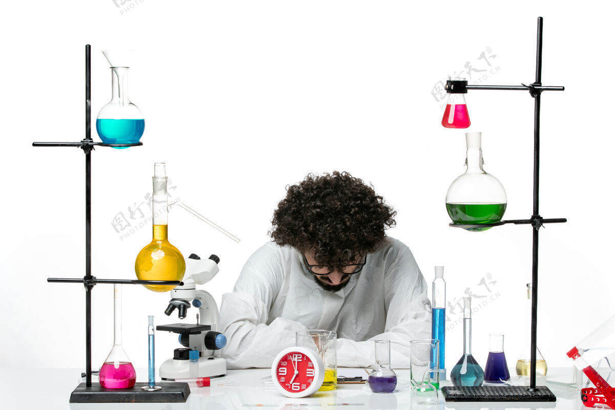 烧杯正面图身着特殊套装的年轻男性科学家坐在白墙上 拿着解决方案瓶子套装容器
