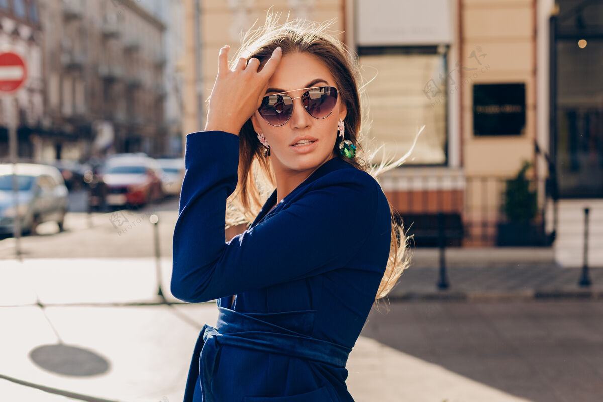 西装在阳光明媚的夏日 穿着蓝色西装戴着墨镜走在街上的性感时尚女人的肖像包魅力优雅