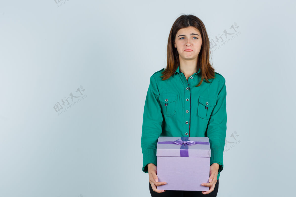 抑郁年轻女孩拿着礼品盒 穿着绿色上衣 黑色裤子 看上去很失望正面图表情坏女人