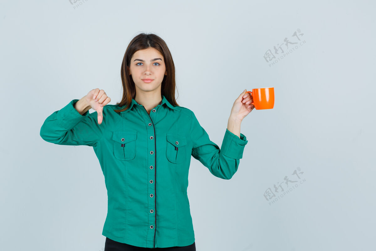 女士年轻女士拿着一杯桔黄色的茶 大拇指朝下穿衬衫 看起来很不满意正面图水疗感性护理
