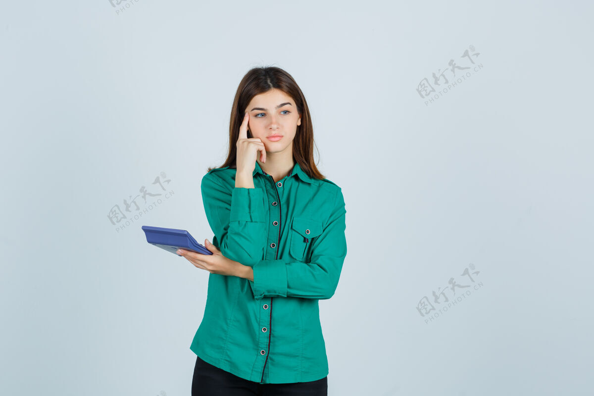 悲伤年轻的女士拿着计算器 手指放在太阳穴上 身穿绿色衬衫 神情沉思 俯视前方客厅手指思考