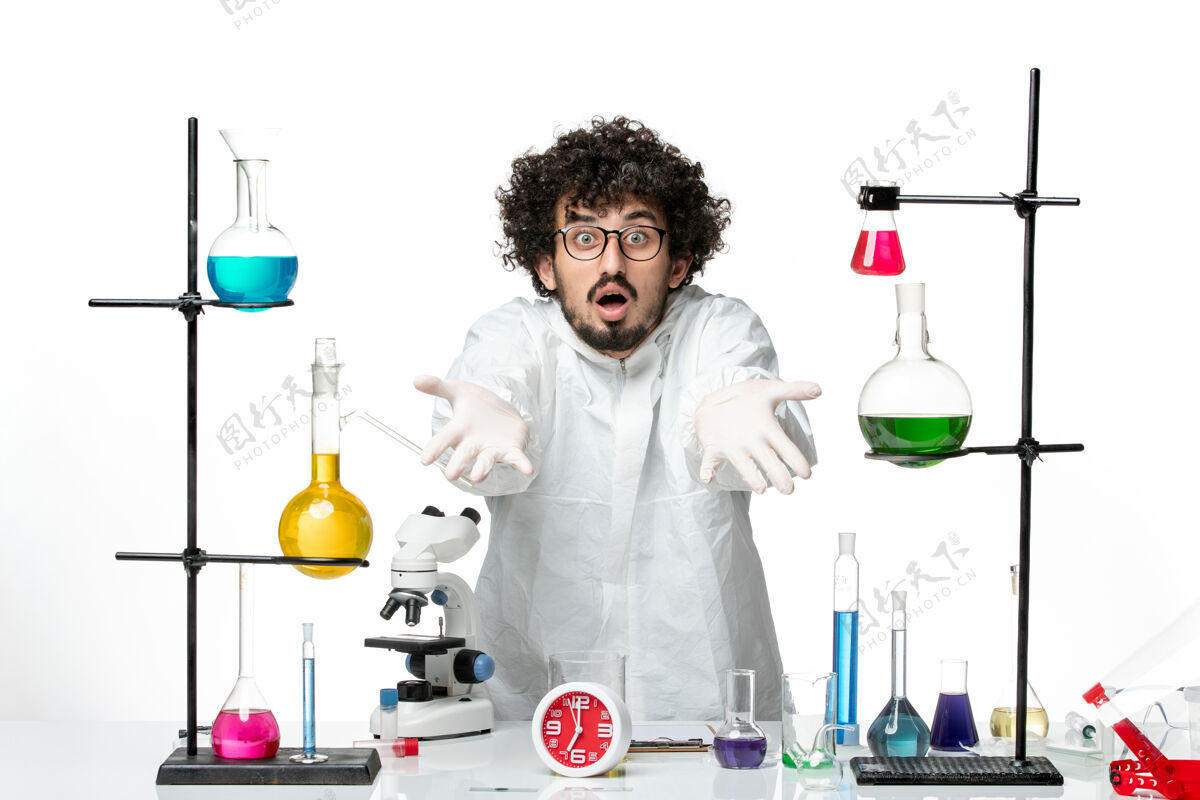 溶液正面图身着特殊套装的年轻男性科学家站在桌子周围 白色墙壁上有解决方案支架套装实验室