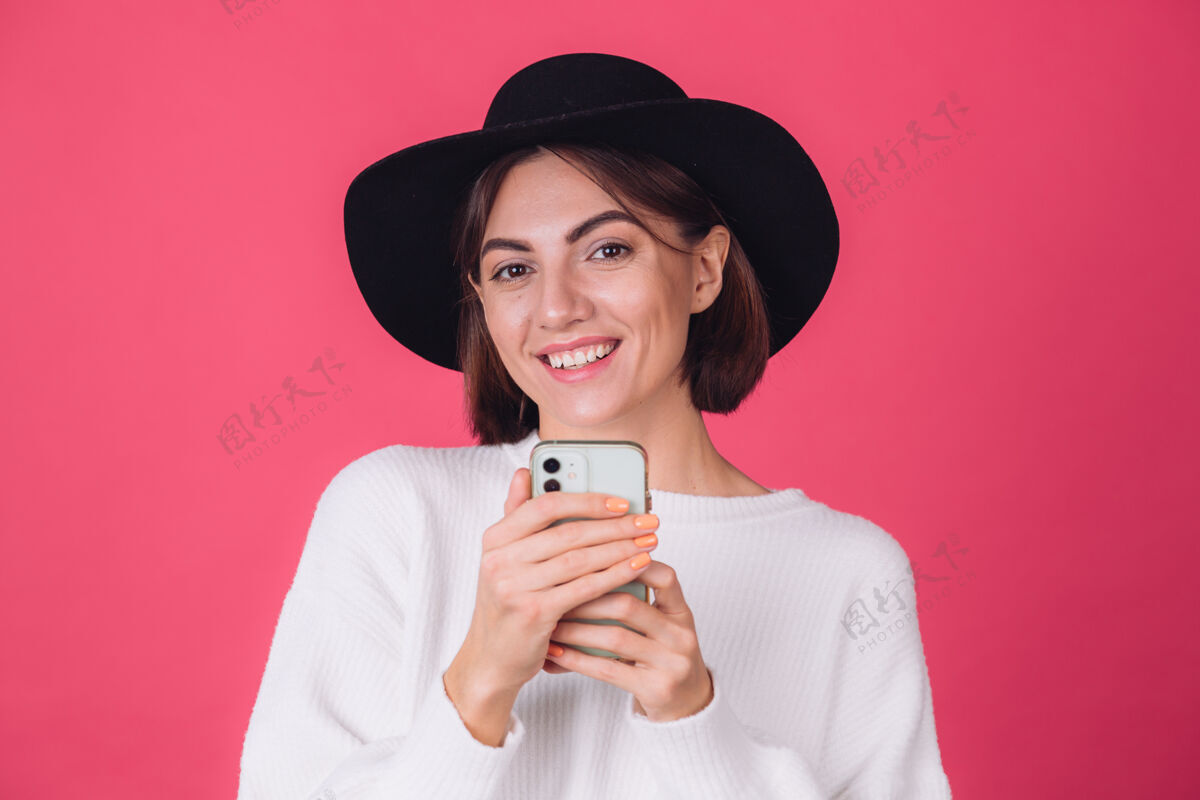 信息穿着白色休闲毛衣 戴着红粉色帽子的时髦女人魅力快乐微笑