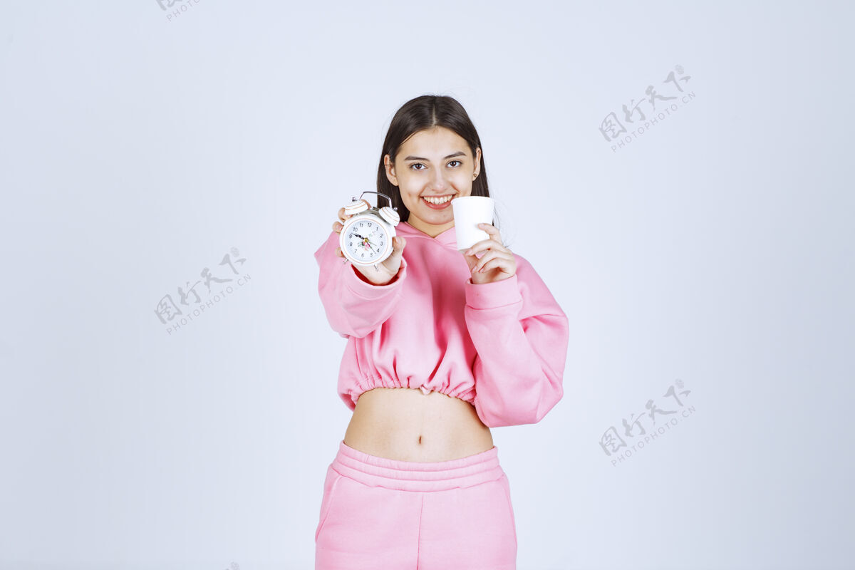 人体模特穿着粉色睡衣的女孩手里拿着闹钟和一杯咖啡年轻积极人