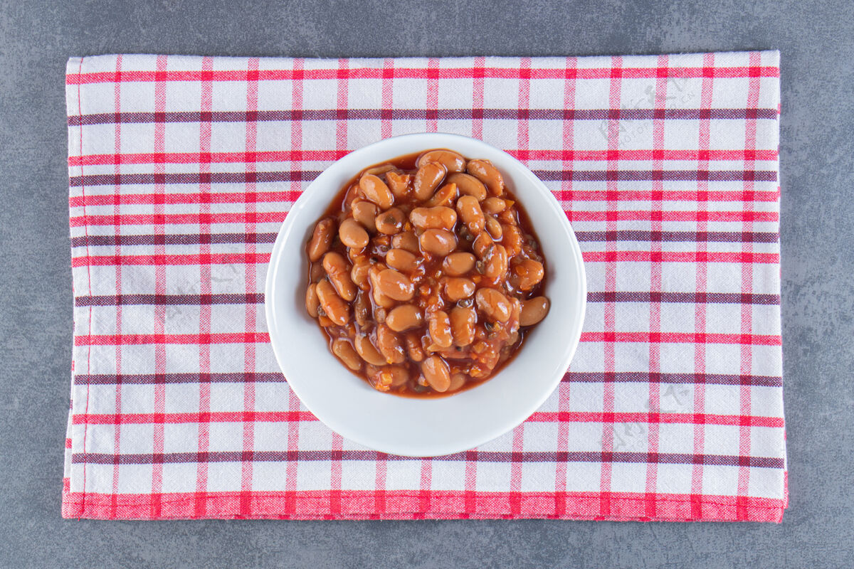 豆子美味的一碗烤豆子放在茶巾上 放在蓝色的表面上好吃的自制的好吃的