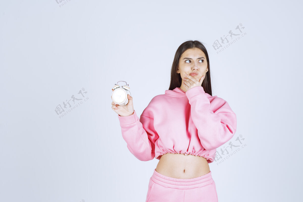 休闲穿着粉色睡衣的女孩手里拿着闹钟 看上去若有所思 不知所措人体模特雇员晋升