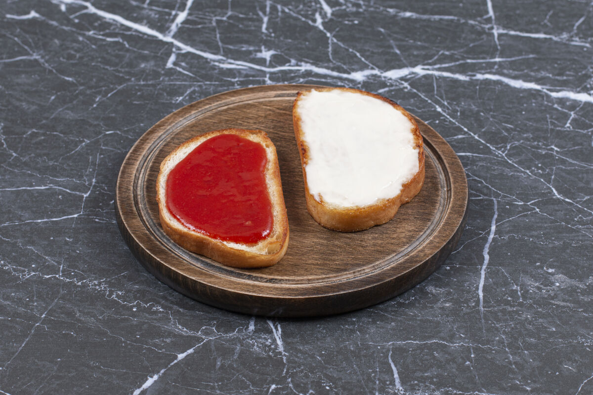 食宿把果酱和奶酪放在两片面包上 放在木板上 放在大理石表面风味烘焙切片