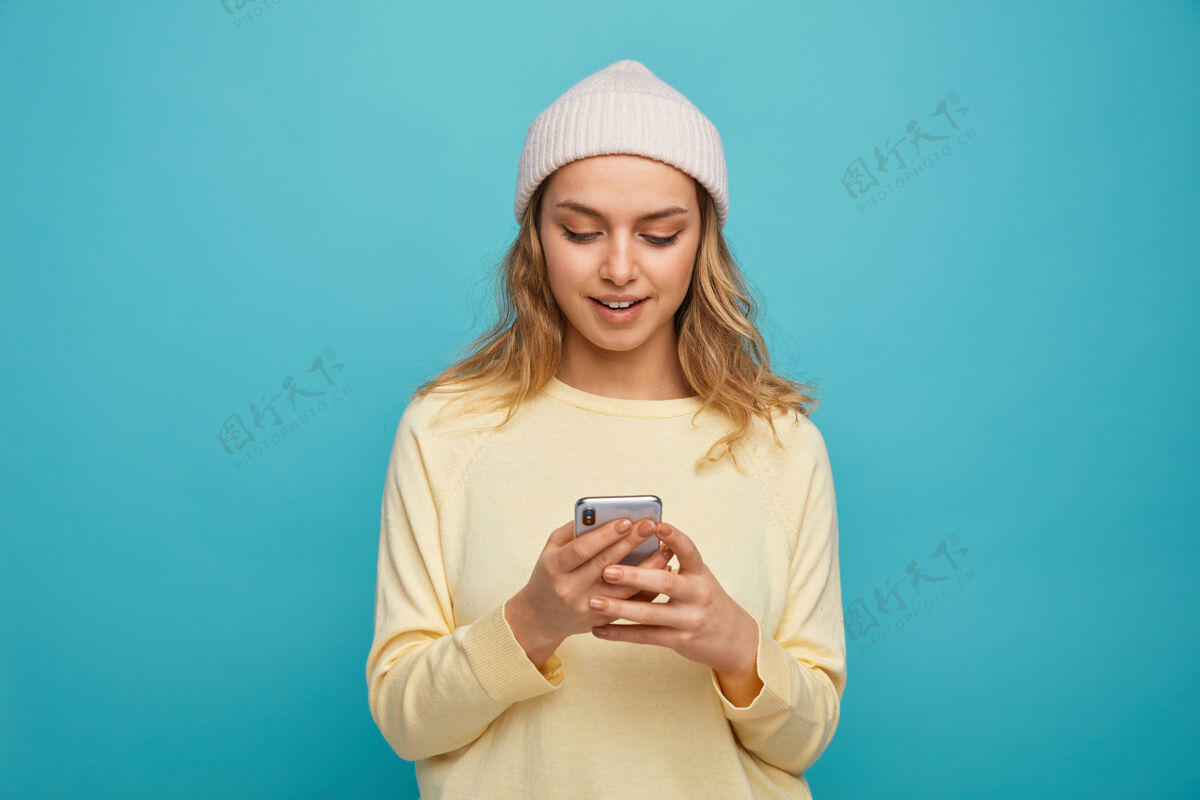 蓝色兴奋的年轻女孩戴着冬天的帽子用她的手机用女孩兴奋