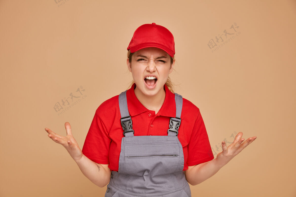 奶油愤怒的年轻女建筑工人穿着制服 戴着帽子喊叫 双手空空帽子手建筑