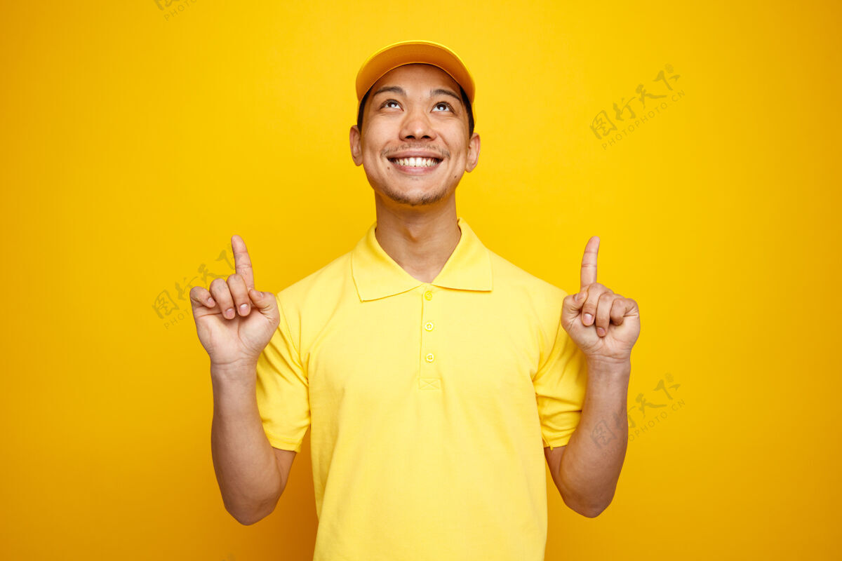 黄色带着微笑的年轻送货员戴着帽子 穿着制服 抬头看着向上交货穿