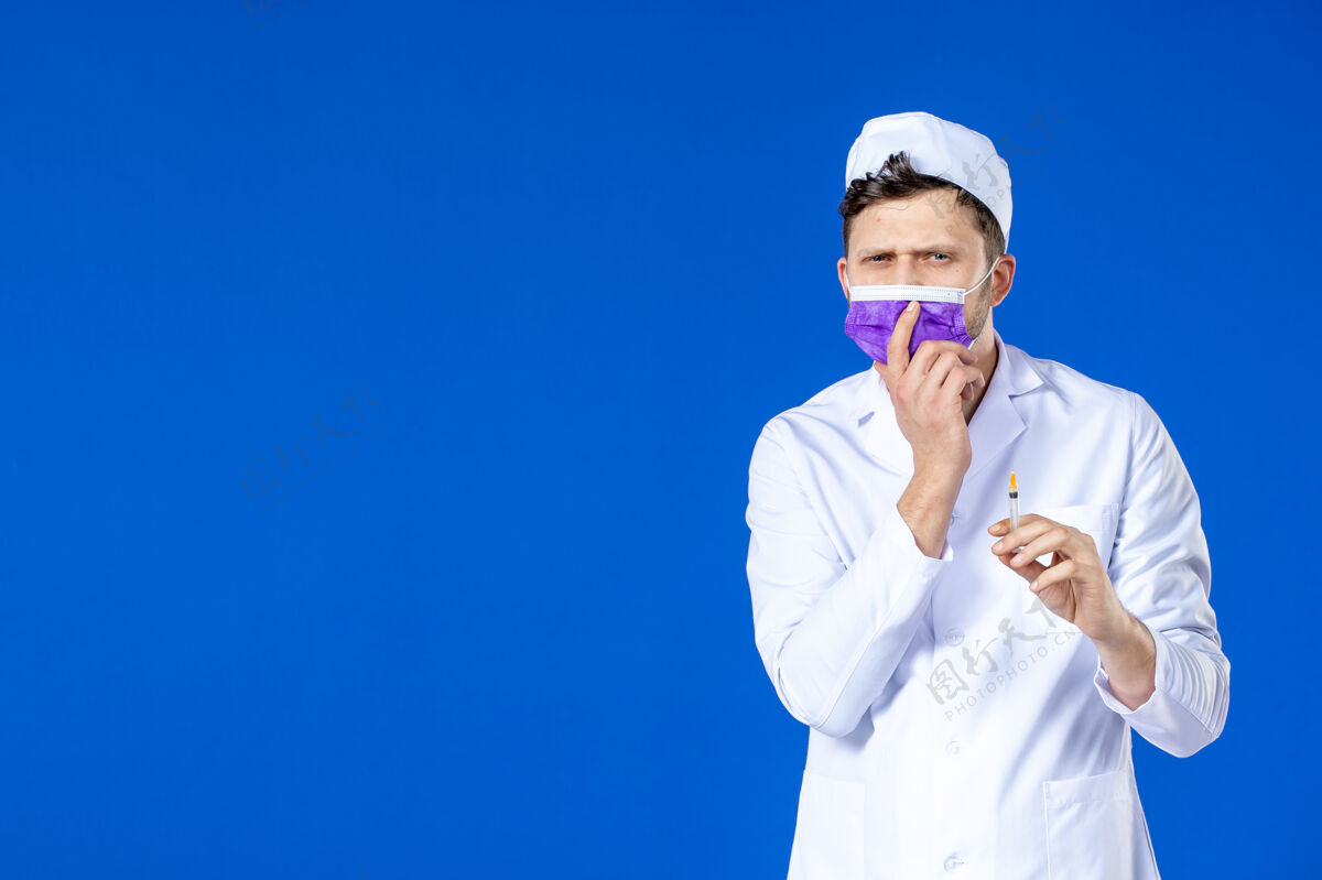 实验室外套身穿医疗服 戴着紫色口罩的男医生正对着蓝色的脸拿着针剂病毒药品注射