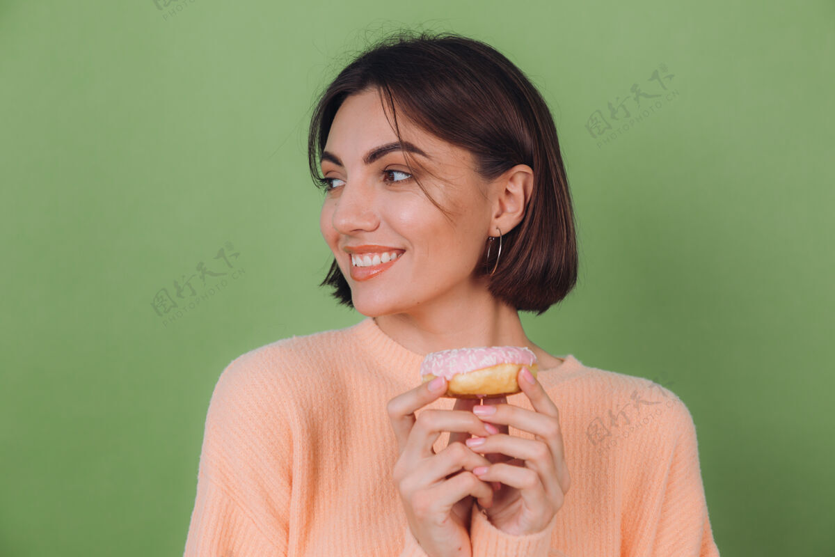 肖像穿着休闲桃色毛衣的年轻时尚女性 隔离在绿色橄榄色墙壁上 粉色甜甜圈快乐复制空间快乐漂亮饥饿
