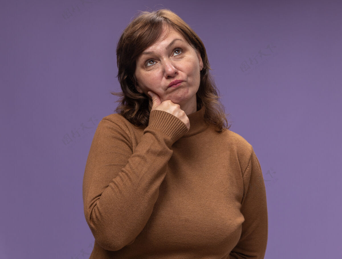 中年身穿棕色套头衫的中年妇女站在紫色的墙上 困惑地抬头望去年龄站拼图