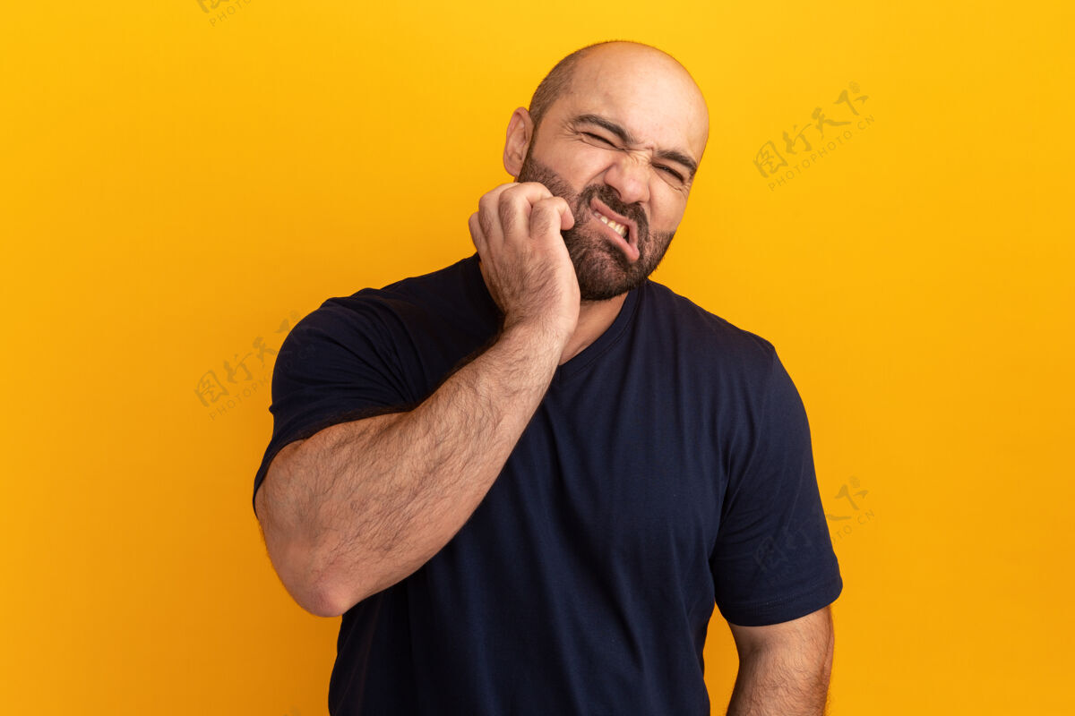 胡子一个留着胡子的男人穿着海军t恤 站在橘色的墙上抓着脸 看起来很困惑站起来困惑伙计