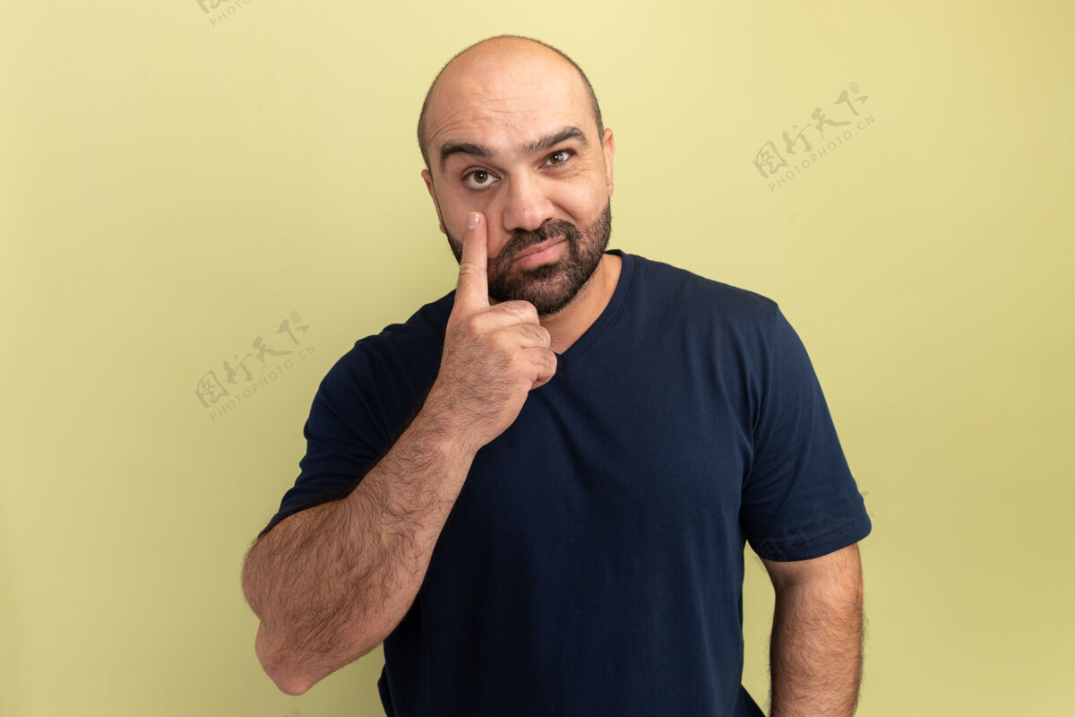 手势身穿黑色t恤的大胡子男人微笑着用食指指着他站在绿色墙上的眼睛站立手指胡须