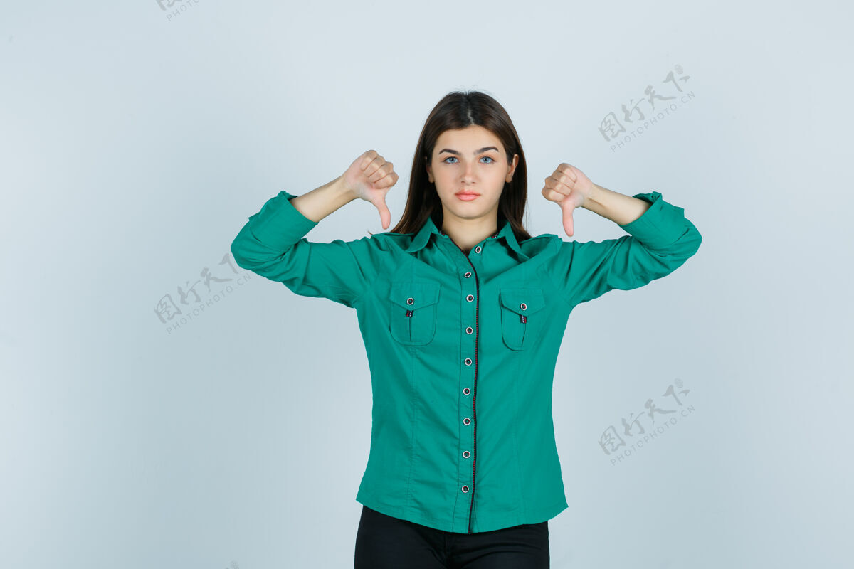 人年轻女性穿着绿色衬衫 双拇指朝下 看起来很不高兴 正面视图痛苦人年轻