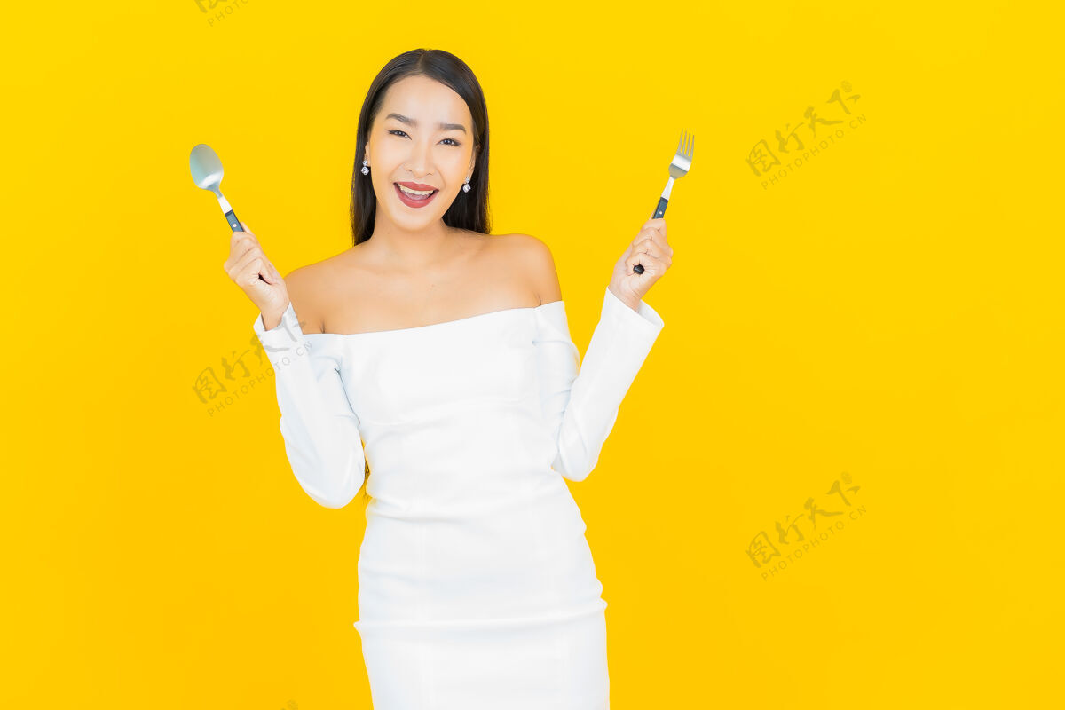 亚洲人在黄色的墙上 一位年轻的亚洲商界美女拿着勺子和叉子准备吃东西欢呼盘子美丽