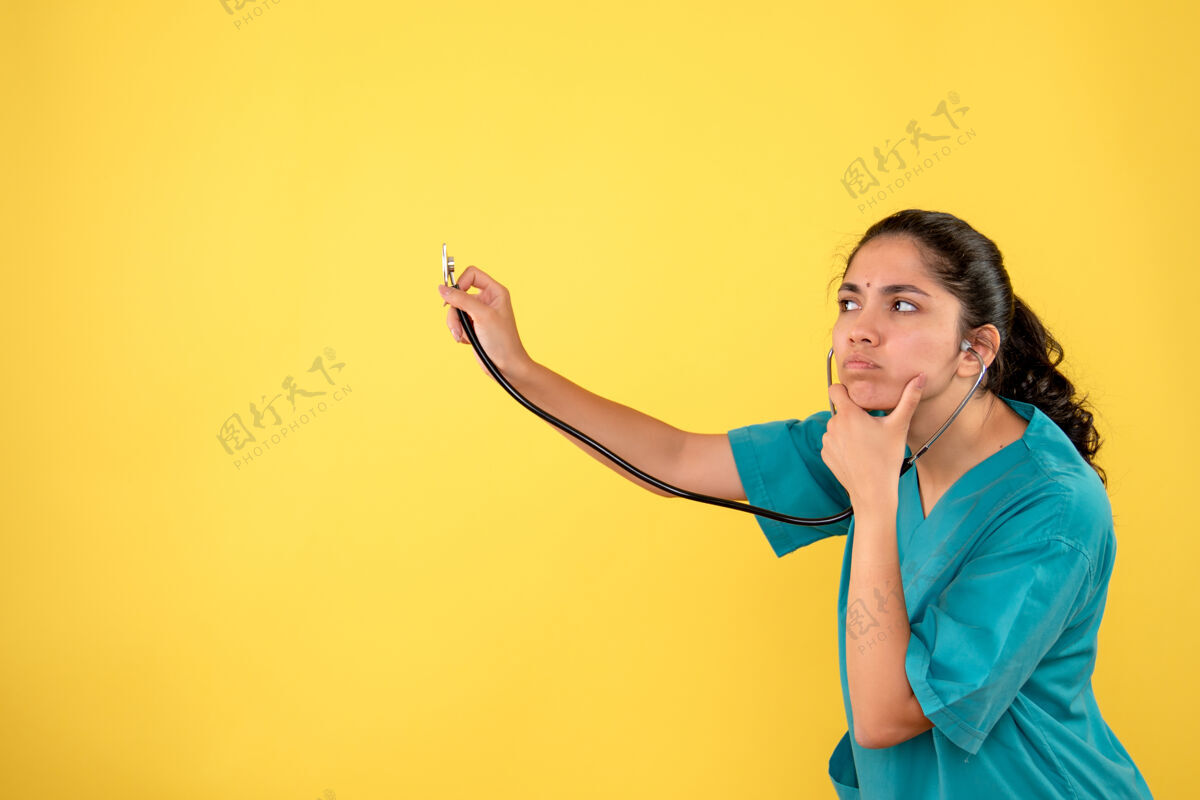 前面前视图体贴的女医生穿着制服在黄色背景上使用听诊器商业微笑听诊器