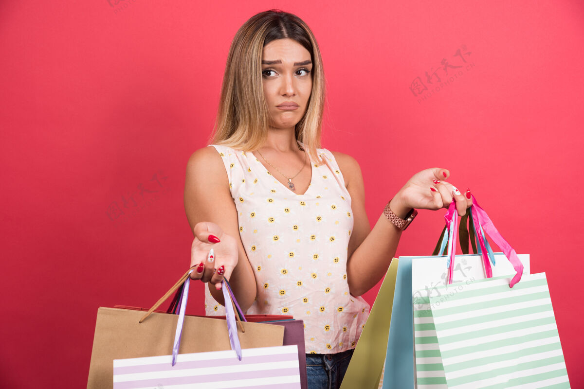 女士红墙上背着购物袋表情悲伤的女人包携带购物者