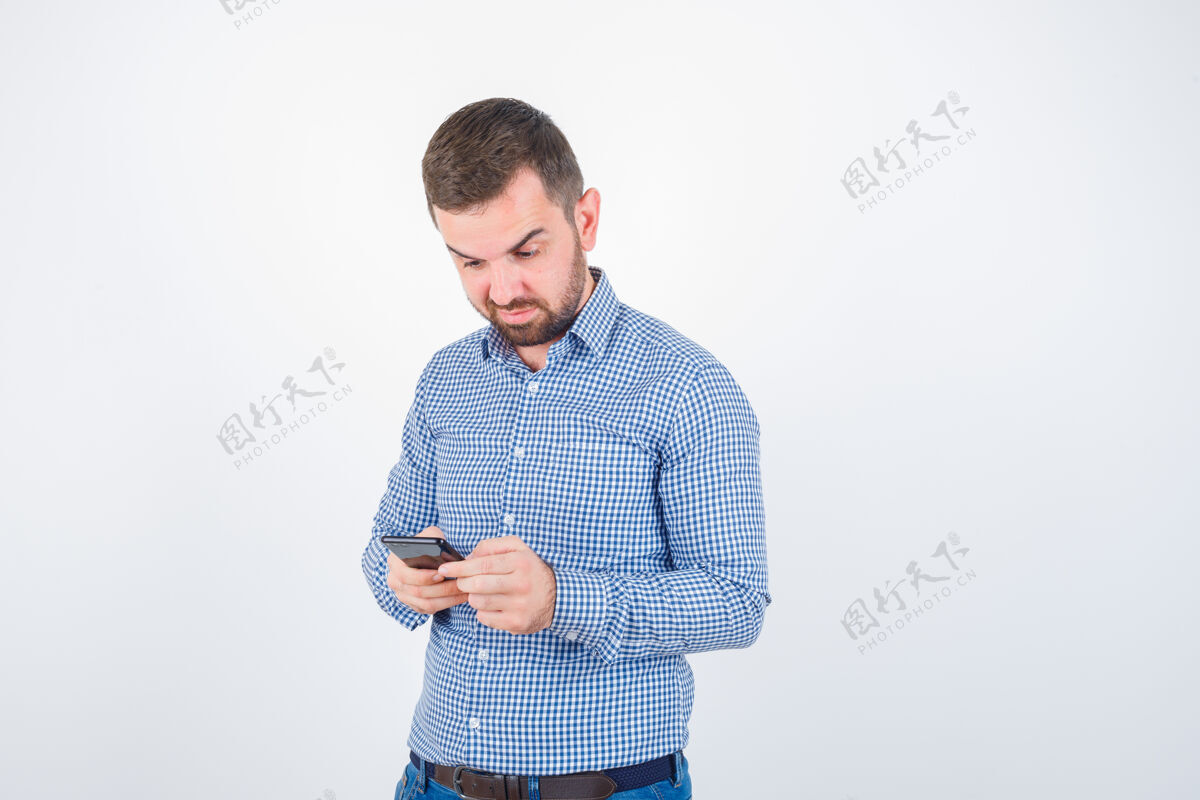 帅哥年轻男子穿着衬衫 牛仔裤在手机上聊天 神情犹豫不决困惑室内聊天