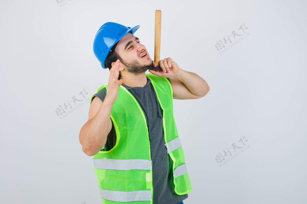 牙科年轻的建筑工人穿着工装 手里拿着锤子 一边举手 看上去很高兴 正对着窗外男孩高兴正面