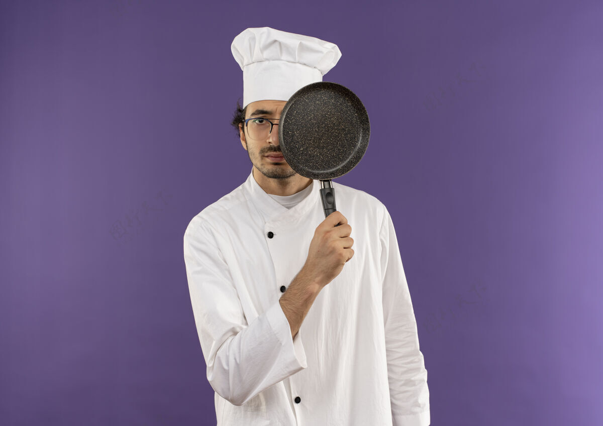 盖年轻的男厨师穿着厨师制服 戴着眼镜 用平底锅遮住眼睛薯条紫色眼睛