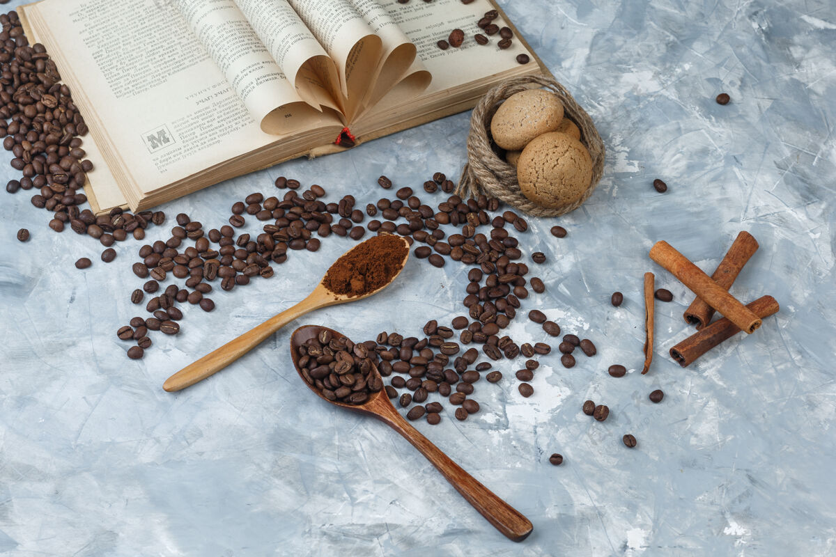 肉桂平铺咖啡豆 速溶咖啡 放在木制勺子里 上面有书 肉桂 饼干 绳子 背景是深蓝色和浅蓝色的大理石水平勺子咖啡因想法