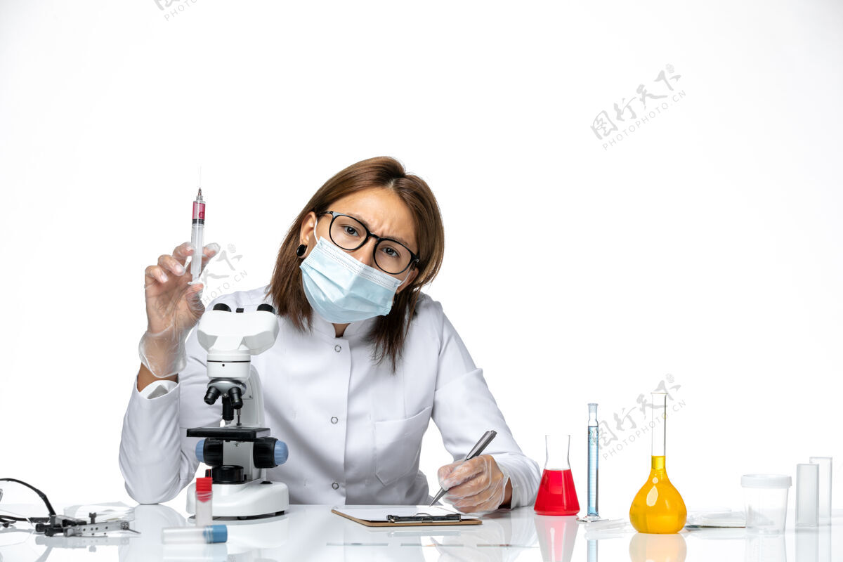 实验室外套前视图：女医生穿着白色医疗服 戴着面罩 因为covid在浅白的空间里拿着针剂面罩医疗到期