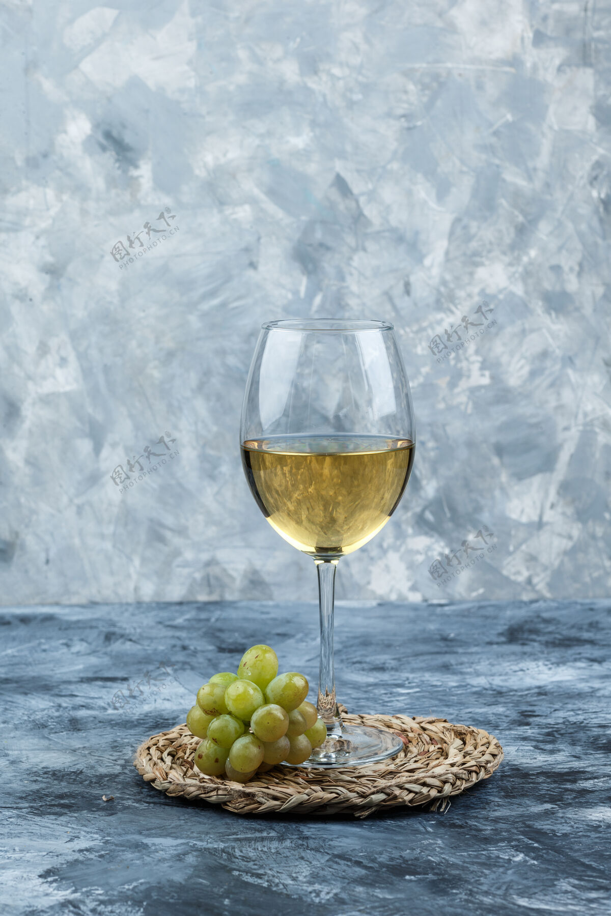 新鲜绿色的葡萄和一杯葡萄酒的侧视图在肮脏的石膏和柳条垫子的背景下树枝路径葡萄